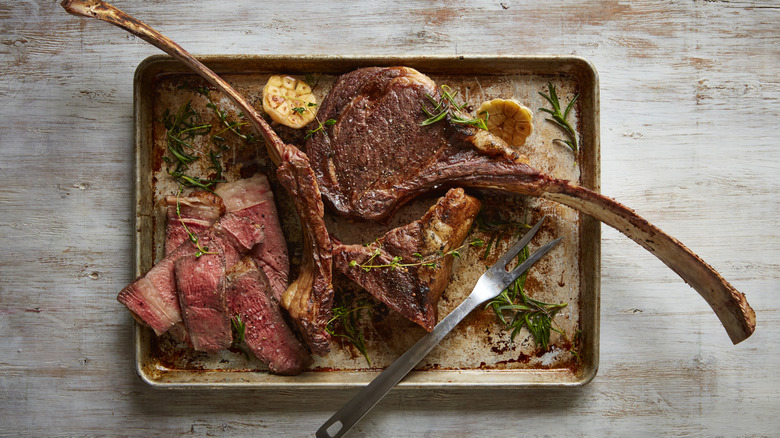 Tomahawk steak on a pan with lemons and herbs