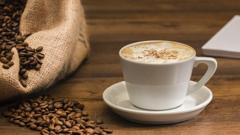 bag of coffee beans with white cup and saucer with cappuccino