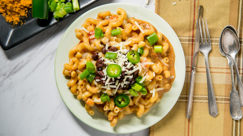 A top-down view of taco mac topped with beans, cheese, peppers, and onions