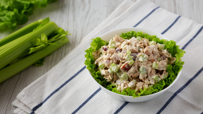 A bowl of chicken salad, looking from above, on a blue and white striped towel and celery sticks to the side