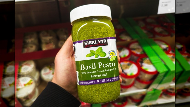 Hand holding jar of Kirkland Signature pesto inside Costco store