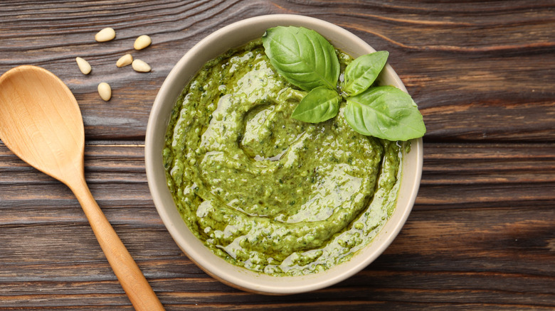 Top view of a bowl of pesto garnished with basil leaves on a wooden surface