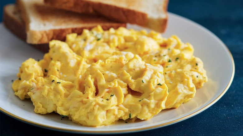 A close-up of creamy scrambled eggs on a plate next to slices of toast