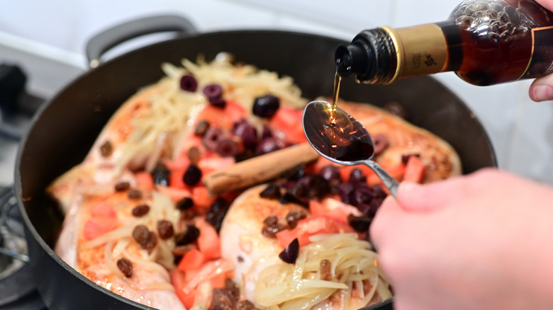Sherry vinegar being poured from a bottle onto a spoon above a Spanish chicken dish cooking in a pan