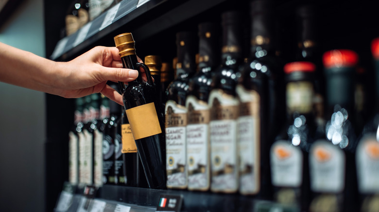 A person's hand picking a bottle of vinegar from a grocery store shelf