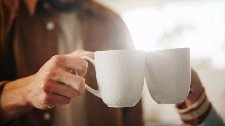 Two people cheersing with white mugs