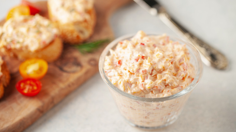 Jar of pimento cheese next to a wooden board with bruschetta
