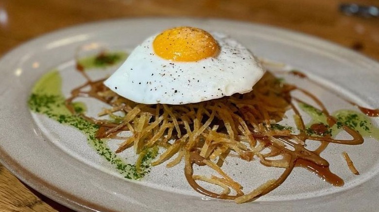A dish of roasted pig, potato sticks, and a fried egg, presented on a gray plate.