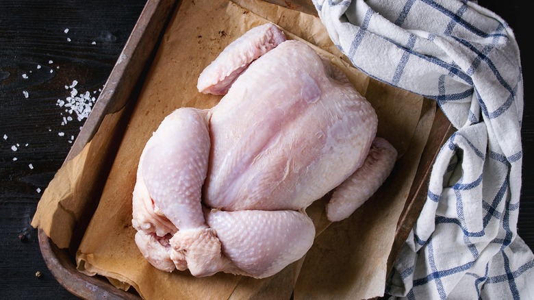 Whole raw chicken on oven tray with towel nearby