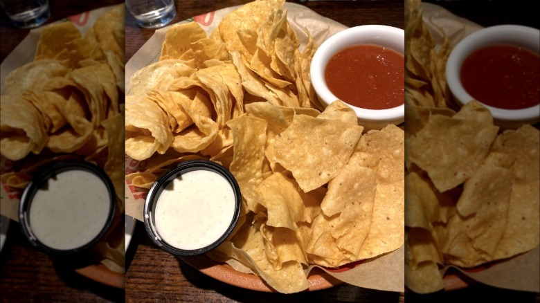 A basket of Chili's tortilla chips with sides of salsa and ranch dressing