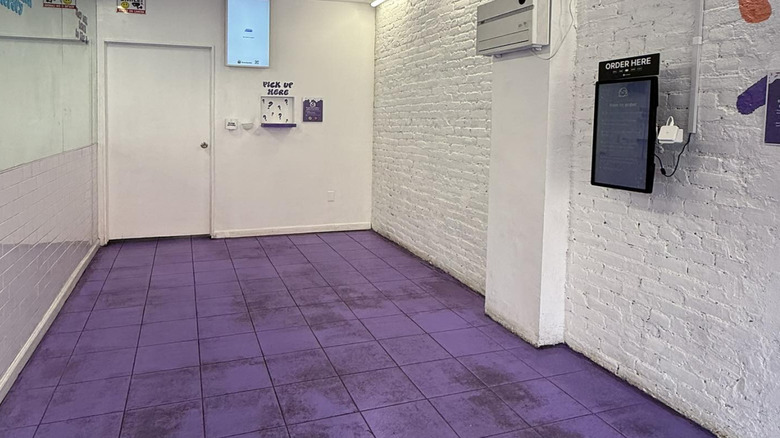 Empty interior with purple floors, white walls, order touchscreen on the wall, and a Pick Up Here window in the back