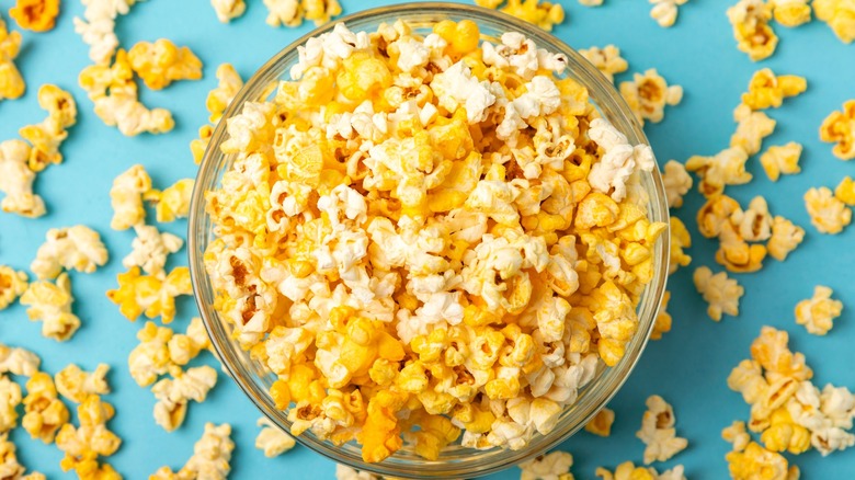 Popcorn in a bowl with popped kernels on a blue background