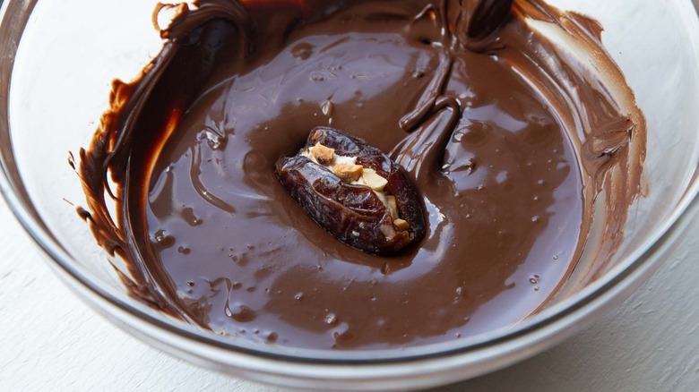 Stuffed date sitting in bowl of melted chocolate