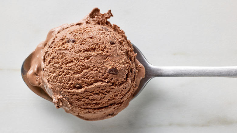 A spoonful of chocolate ice cream hovering over a table.