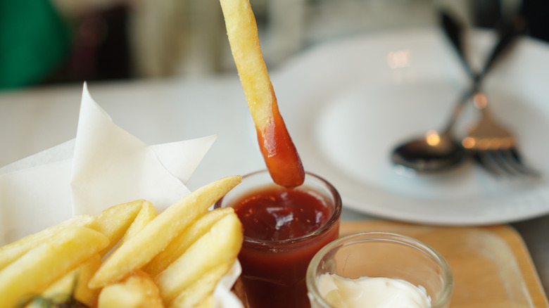 A person dipping a french fry in ketchup.