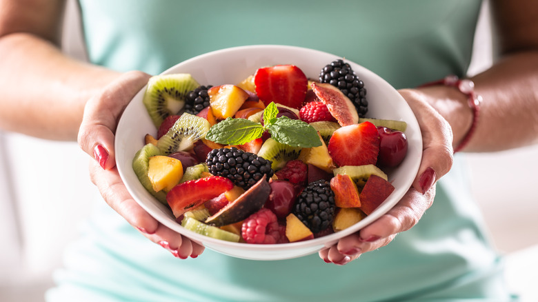 Hands holding a bowl of fruit salad garnished with mint