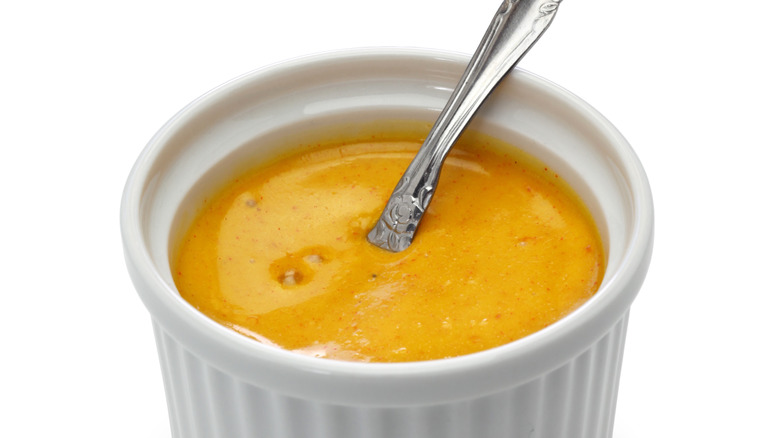 Close-up of orange-yellow sauce in a small white ramekin with a spoon handle sticking out of it