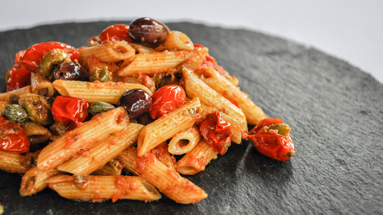 Serving of penne with puttanesca sauce on black platter