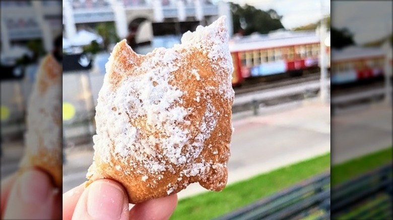 hand holding a beignet in an outdoor setting