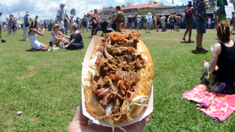 hand holding cochon de lait sandwich in an outdoor setting