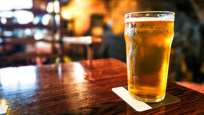 A cold, bright orange beer in a glass on a wooden table inside a pub or restaurant