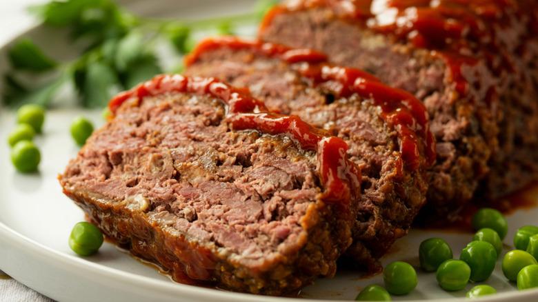 meatloaf on a white plate with peas