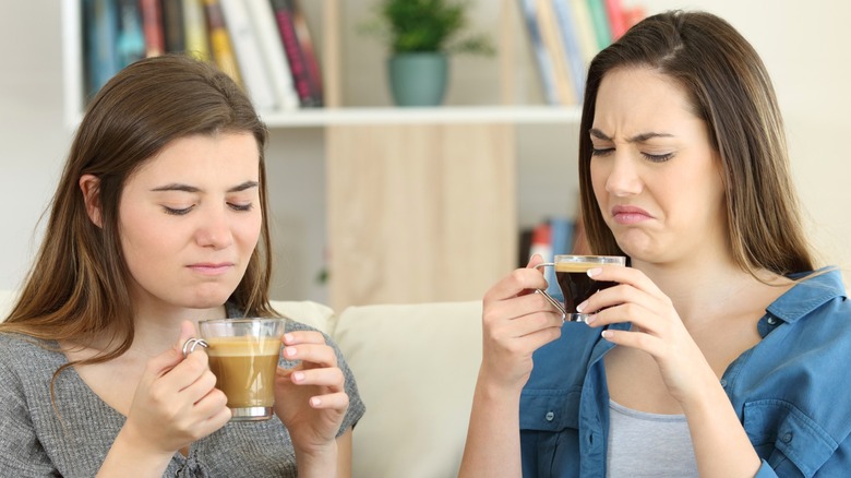Two people drinking coffee on couch with disgusted facial expressions