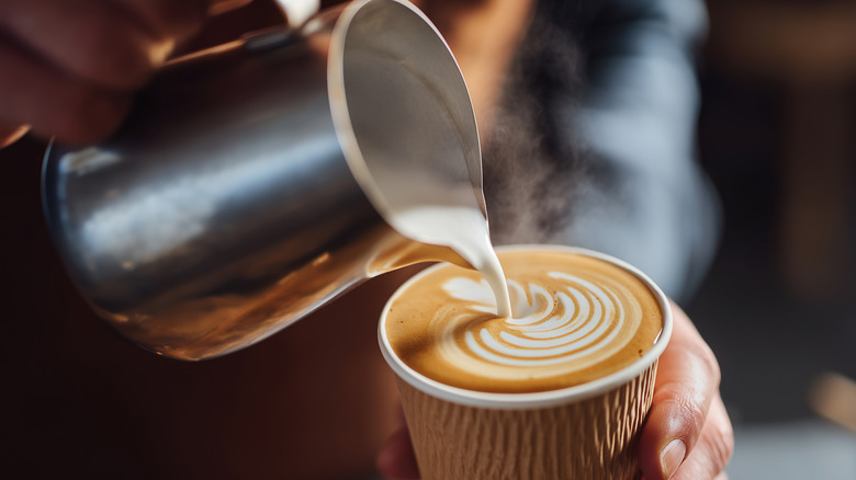 Frothed milk being poured into a paper coffee cup