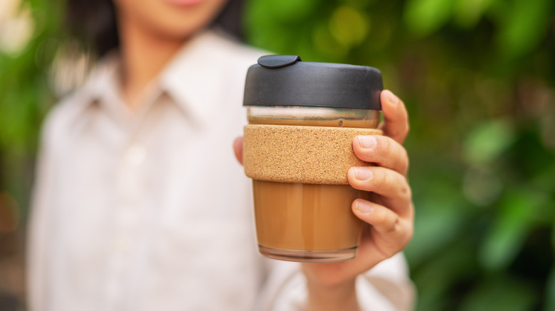 A woman's hand holding a reusable glass coffee mug