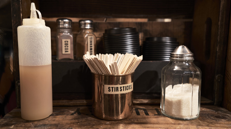 honey, stir sticks, and sugar sitting on a coffee shop condiment bar
