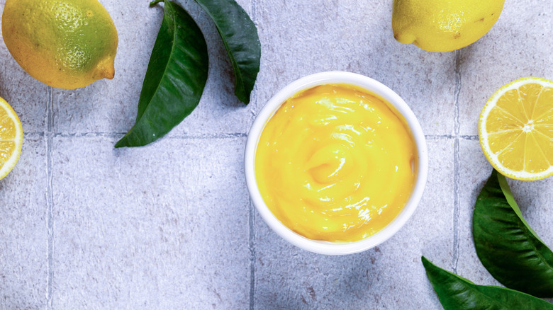 A cup of lemon curd surrounded by lemons and leaves