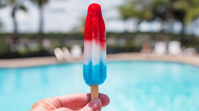 Hand holding Bomb Pop in front of swimming pool