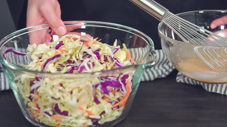 Hands preparing coleslaw in a glass bowl.