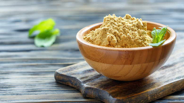 Bowl with mustard powder atop a wooden board on wooden table.