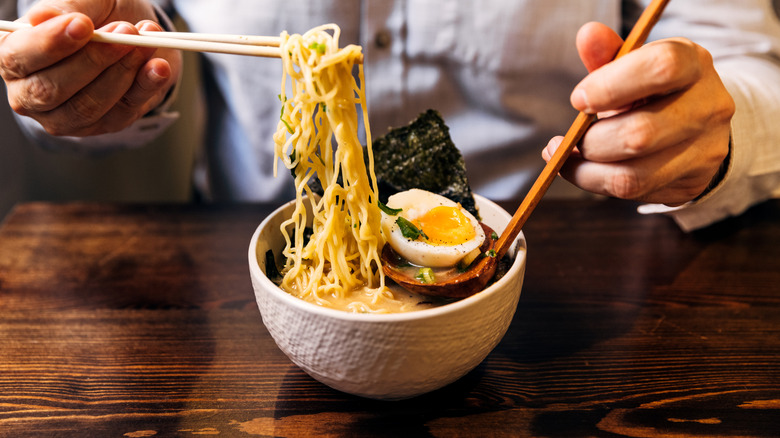 A diner eats a bowl of ramen with a soft-boiled egg