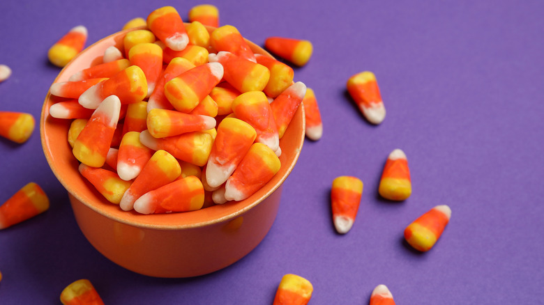 A bowl of candy corn with a purple background