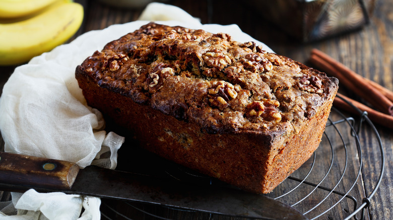Loaf of walnut banana bread on rack next to knife