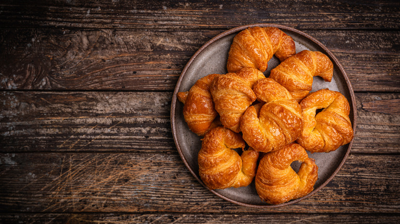 A plate of plain croissants on a farmhouse style table.