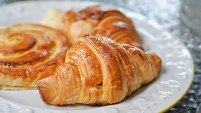 A straight croissant au beurre sitting on a plate with other pastries.