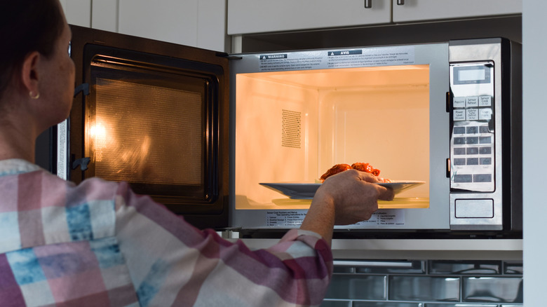 A woman places a plate of leftovers in a microwave