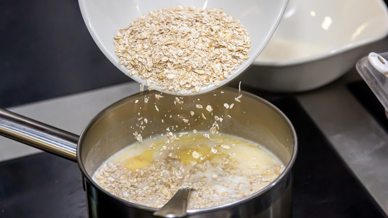 Pouring raw oats into a pot of milk on the stove to make oatmeal