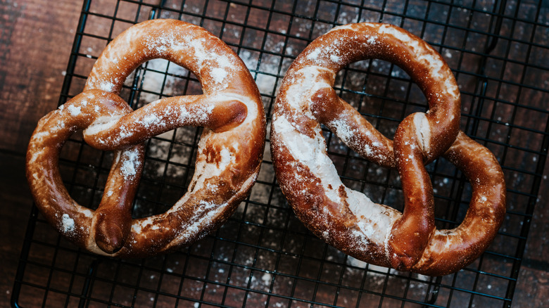 Two soft pretzels sprinkled with powdered sugar rest on a wire rack