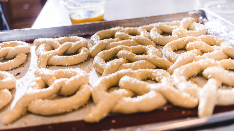 A tray of uncooked soft pretzels sprinkled with salt on a kitchen counter