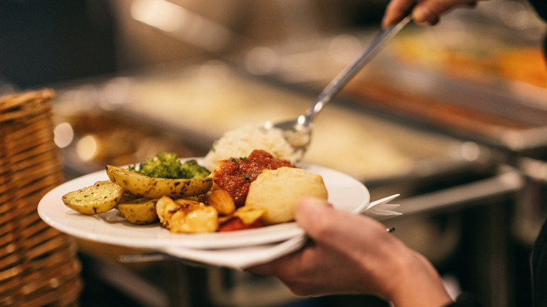 A person using a serving spoon to add food to their buffet plate