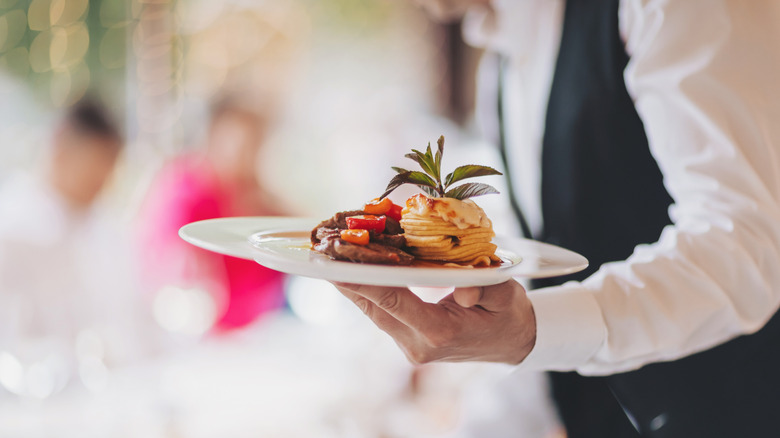 A smartly-dressed server carrying a plate of food to a table