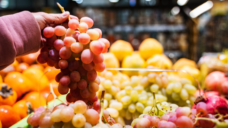 A person holding a bunch of grapes in a market.
