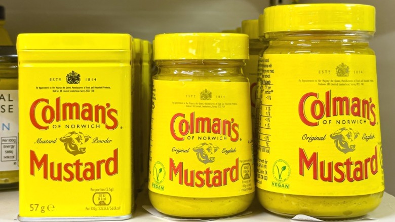 Jars and tins of Colman's mustard on a supermarket shelf.