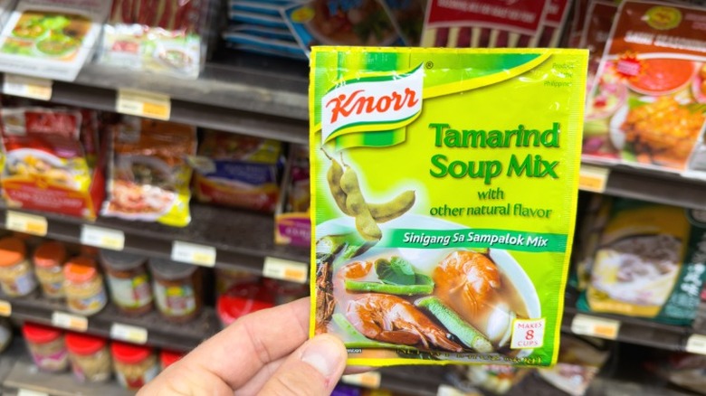 A hand holding a package of Knorr Tamarind soup mix at the supermarket.