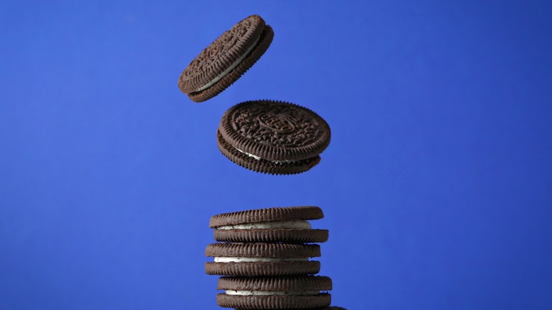 Several Oreos falling into a pile against a blue background.