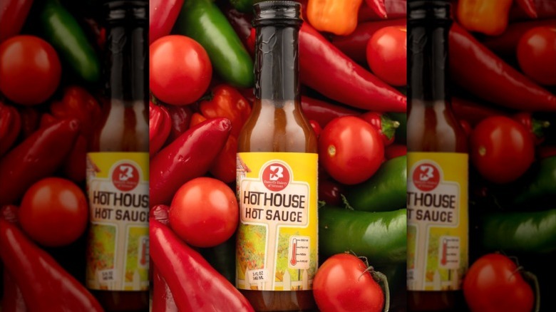 A bottle of Butterfly Bakery Hot House Hot Sauce, surrounded by peppers.